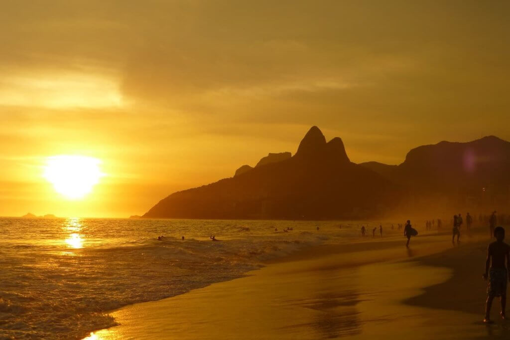 The sun sets with a golden gleam over the mountainous beachside of a Brazilian coastline