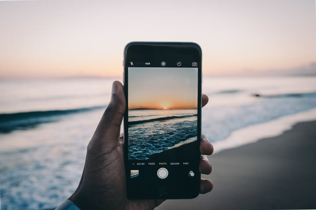 A person holds a smartphone with a picture of a sunset showing on its screen