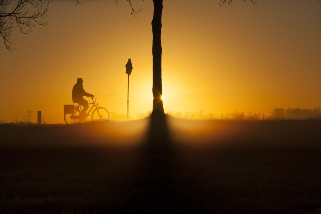A man bikes against the backdrop of a warm sun either ending or starting its daily journey.