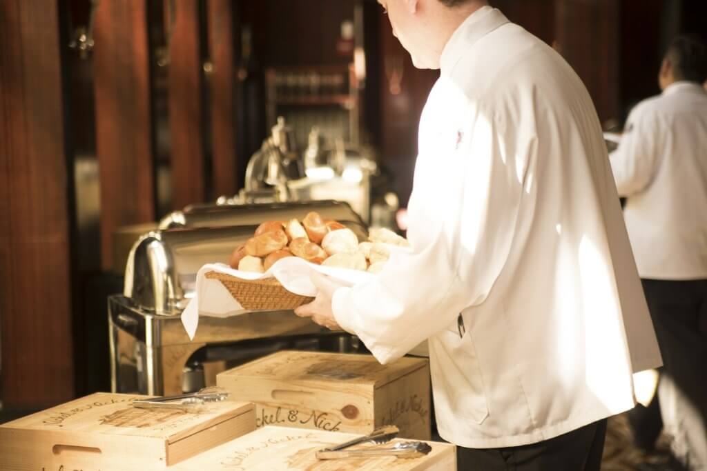 A waiter carrying a basket of potato-sized baked breads.