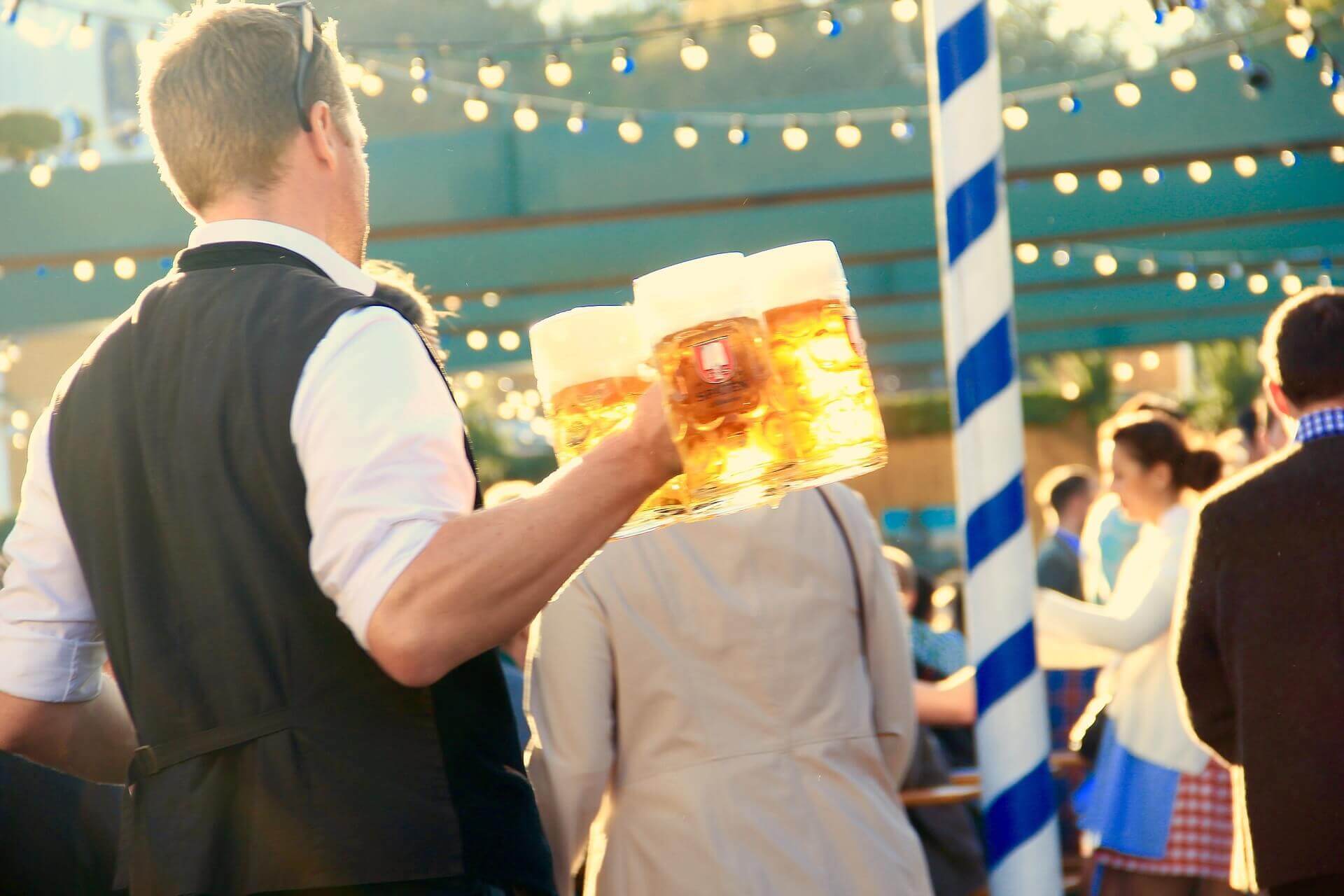 A waiter carrying at least three jugs of beer at a festival.