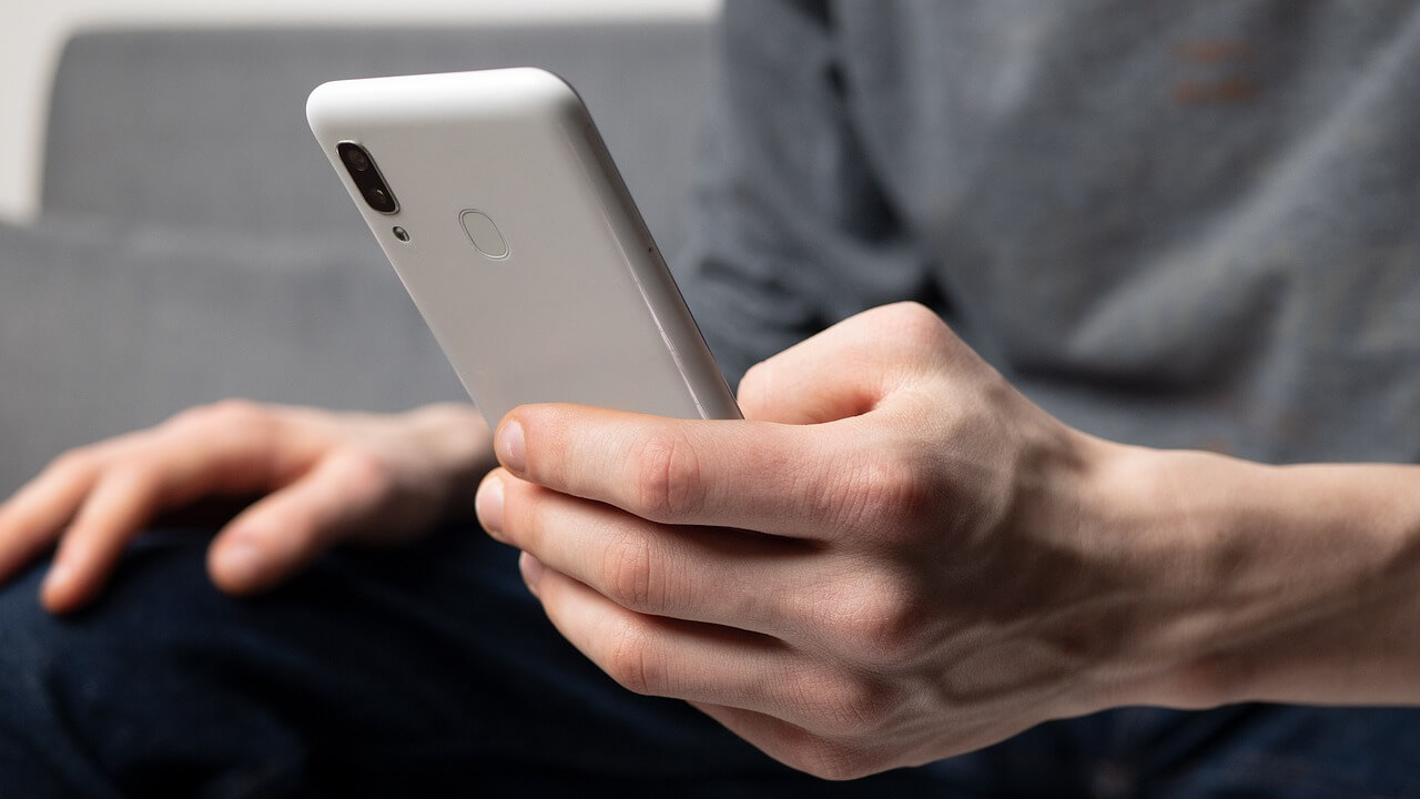 A person holds a smartphone with one hand, either scrolling or clicking on something on the screen with his thumb.