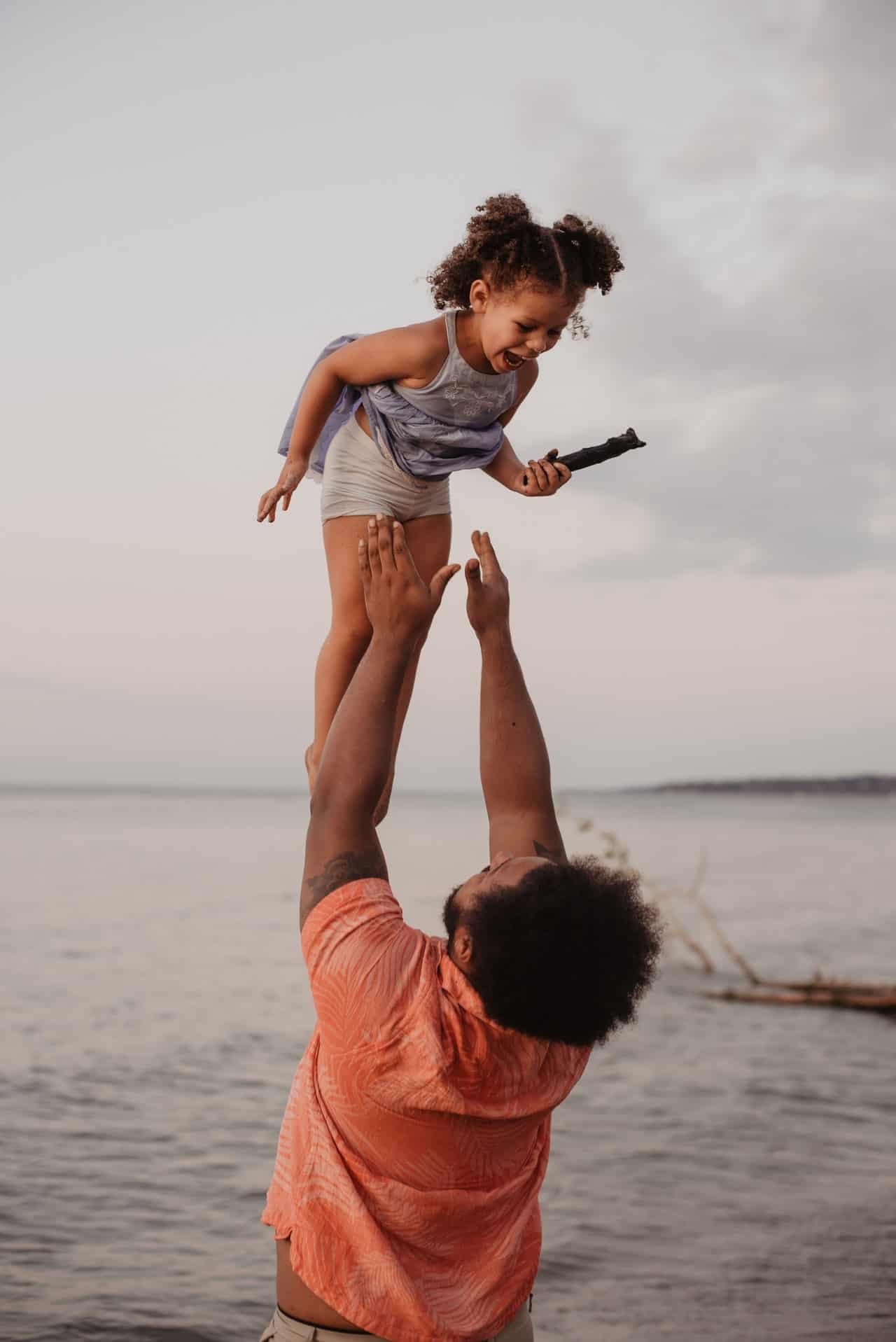 A father launches his daughter in the air with arms outstretched, ready to catch her. 