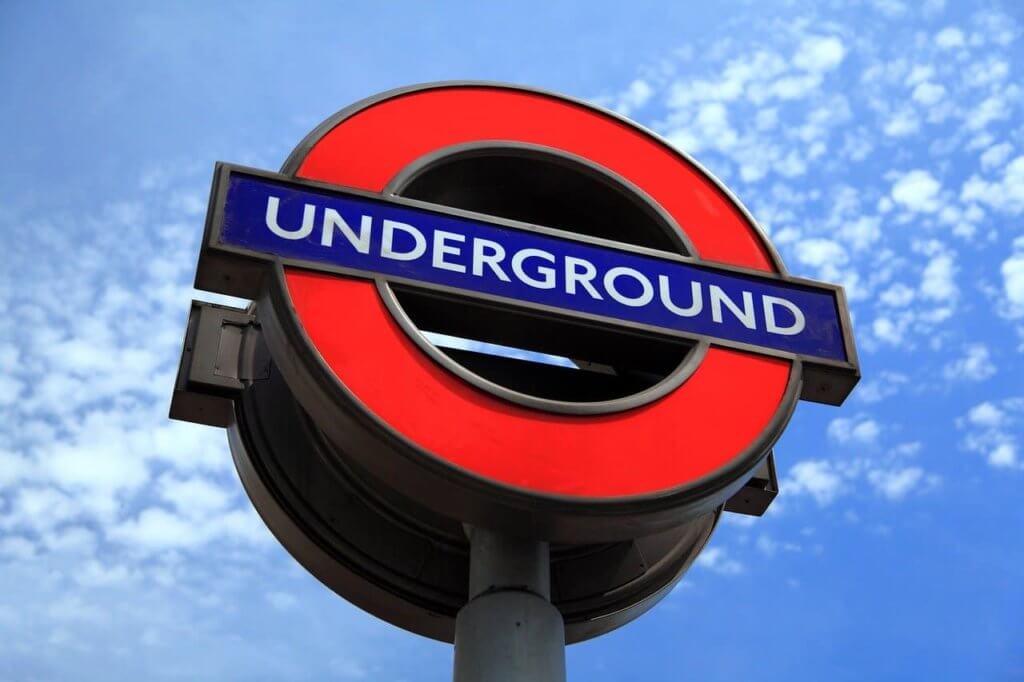 A sign of London's underground stands under a blue sky