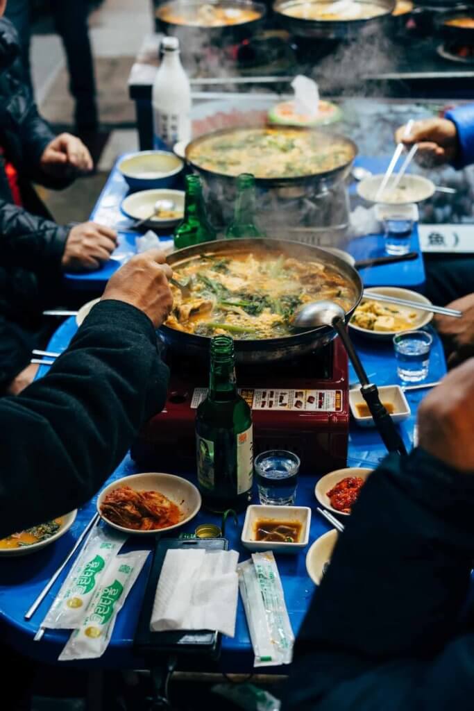 Table with warm Korean dishes; hands stand at the ready
