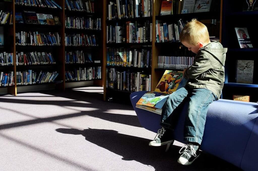 A child sits inside a library, flipping a book