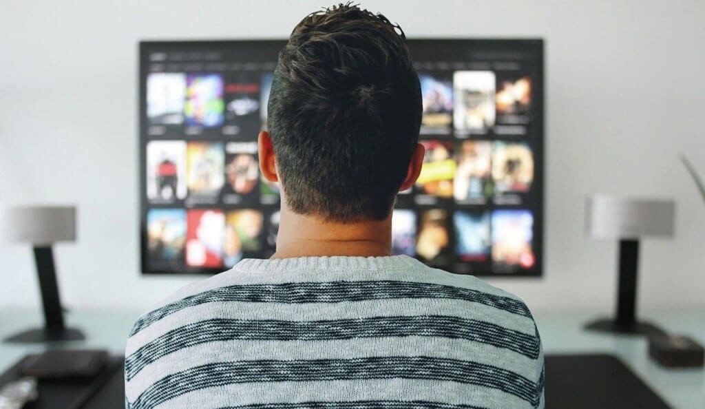 A person stands in front of a TV with the options menu of Netflix on it