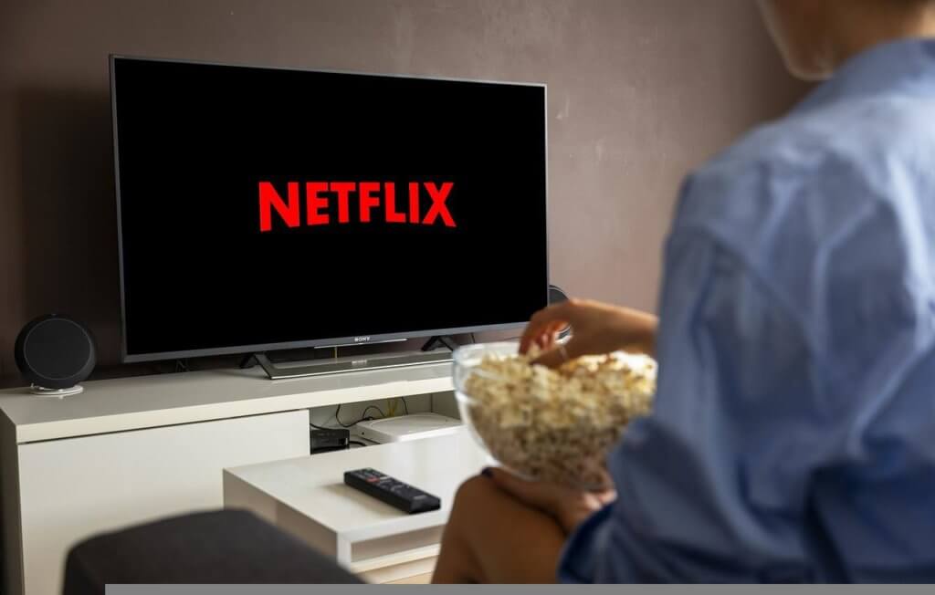 A person holds a bowl of popcorn while watching Netflix