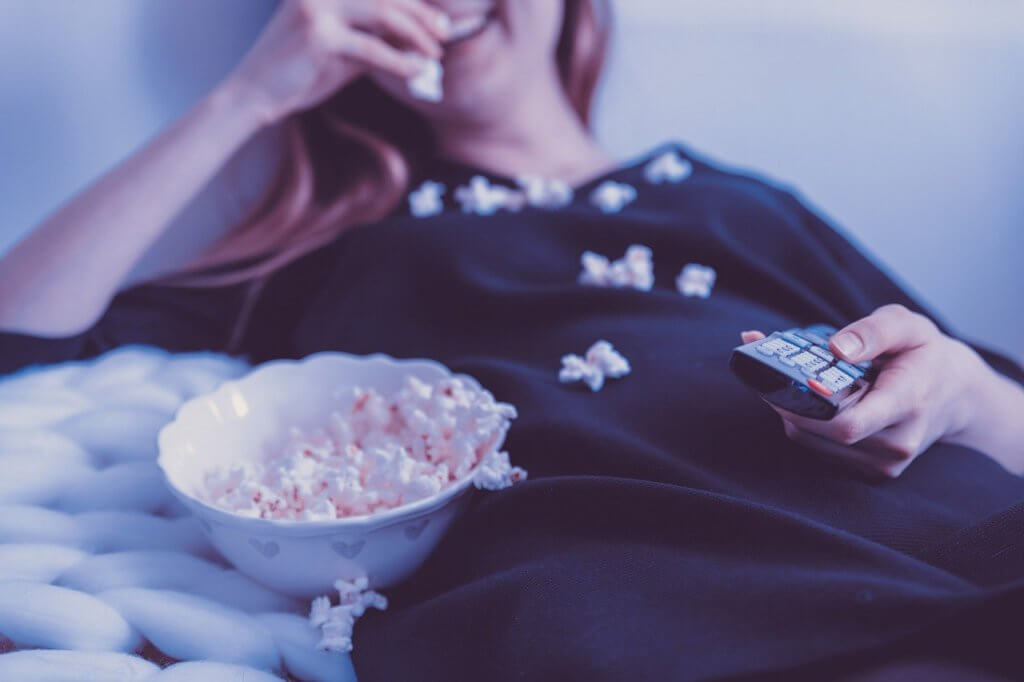 woman eating popcorn from a bowl while holding a TV remote in the other hand