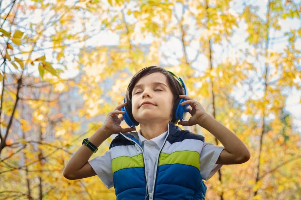 child wearing headphones with eyes closed against an autumnal tree backdrop