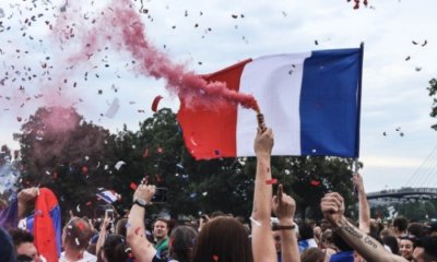 a crowd celebrating with flares, confetti, raised arms and waving a French flag