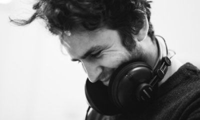 Smiling dark-haired man looks down while wearing headphones around his neck