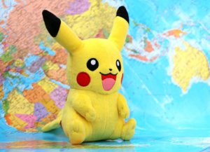 A plush Pikachu doll sits in front of a world map.
